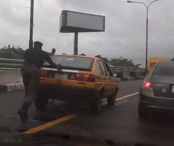 Hmmm!! Policeman Spotted  Helping Taxi Driver To Push His Broken Down Vehicle [See Photo]
